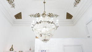 Un lustre à plusieurs lampes, des décorations élaborées au plafond et une porte blanche.