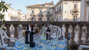 Une table dressée avec des bouteilles de vin et des verres sur un balcon donnant sur des bâtiments historiques.