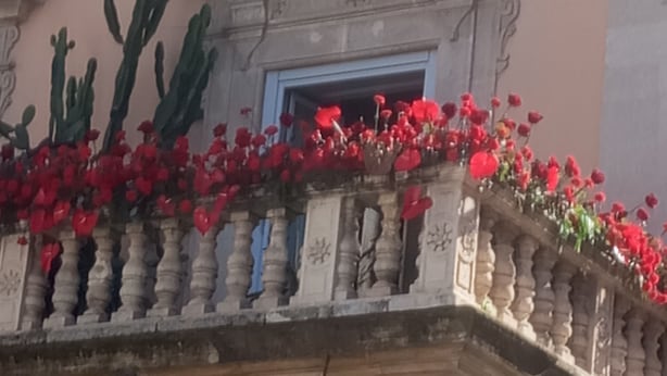 Une façade d’immeuble agrémentée d’un balcon orné de fleurs rouges et de cactus.