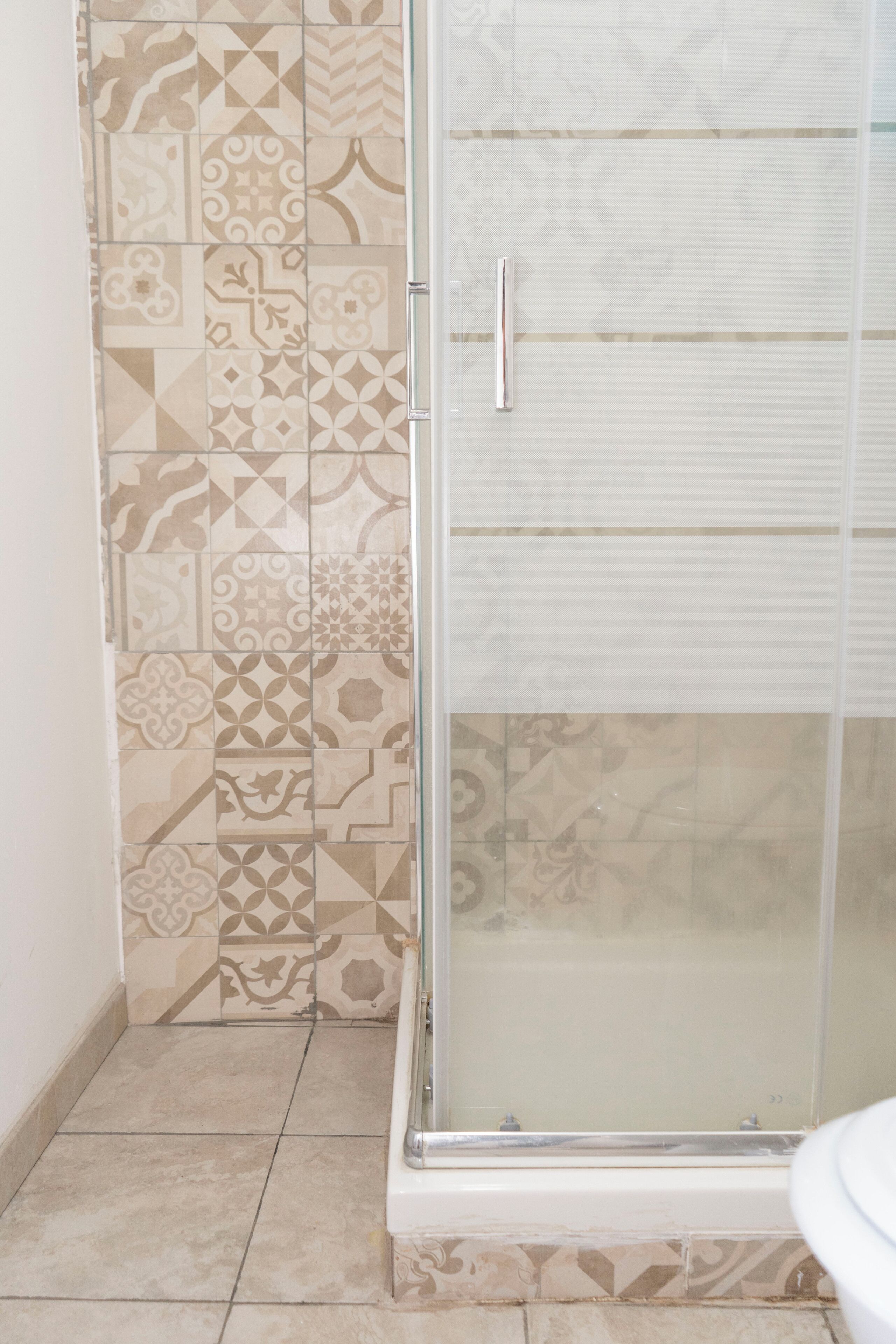 Un bagno con piastrelle decorate, cabina doccia in vetro e un water.