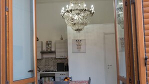 Un espace repas ouvert, agrémenté d’un lustre, d’une table recouverte d’une nappe à motifs et offrant une vue sur la cuisine.