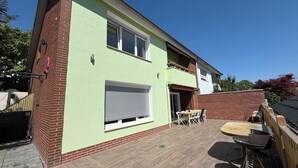 A two-story house with a green exterior, a patio with a table and chairs, and a brick wall.