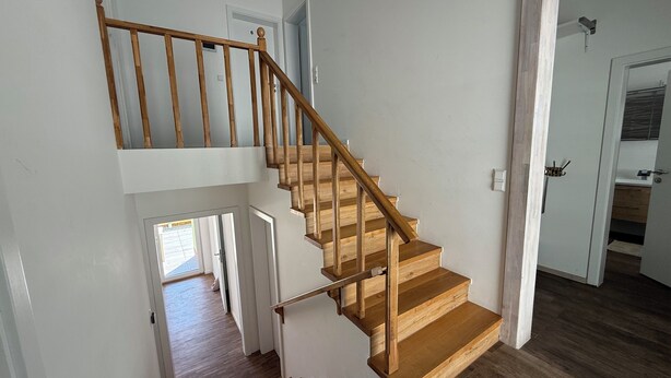 A wooden staircase with a handrail leading to an upper floor.