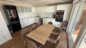 A compact kitchen with white cabinets, a built-in oven, and a dining area with a wooden table and chairs.