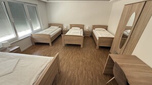 A bedroom with three wooden beds, a large mirror, and a window with blinds.
