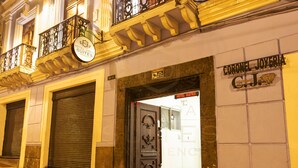 Entrada de hotel con una persiana cerrada, un balcón con barandillas decorativas y un cartel que indica Hotel David Suites.