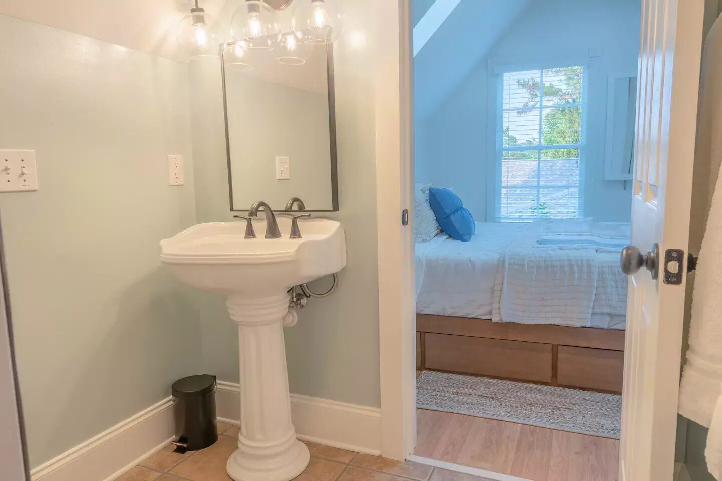 Un baño con lavamanos pedestal, espejo y lámpara.