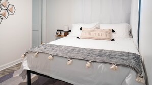 A neatly made bed with a patterned blanket and pillows, a bedside table with a lamp, and a geometric wall decoration. - Minimalist Style Home in Downtown JC - TF #12 (Johnson City)