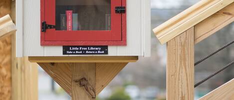 Eine kleine Holzhütte mit roter Tür, beschriftet als „Little Free Library“, mit einem Schild darunter: „Buch mitnehmen – Buch zurückgeben.“
