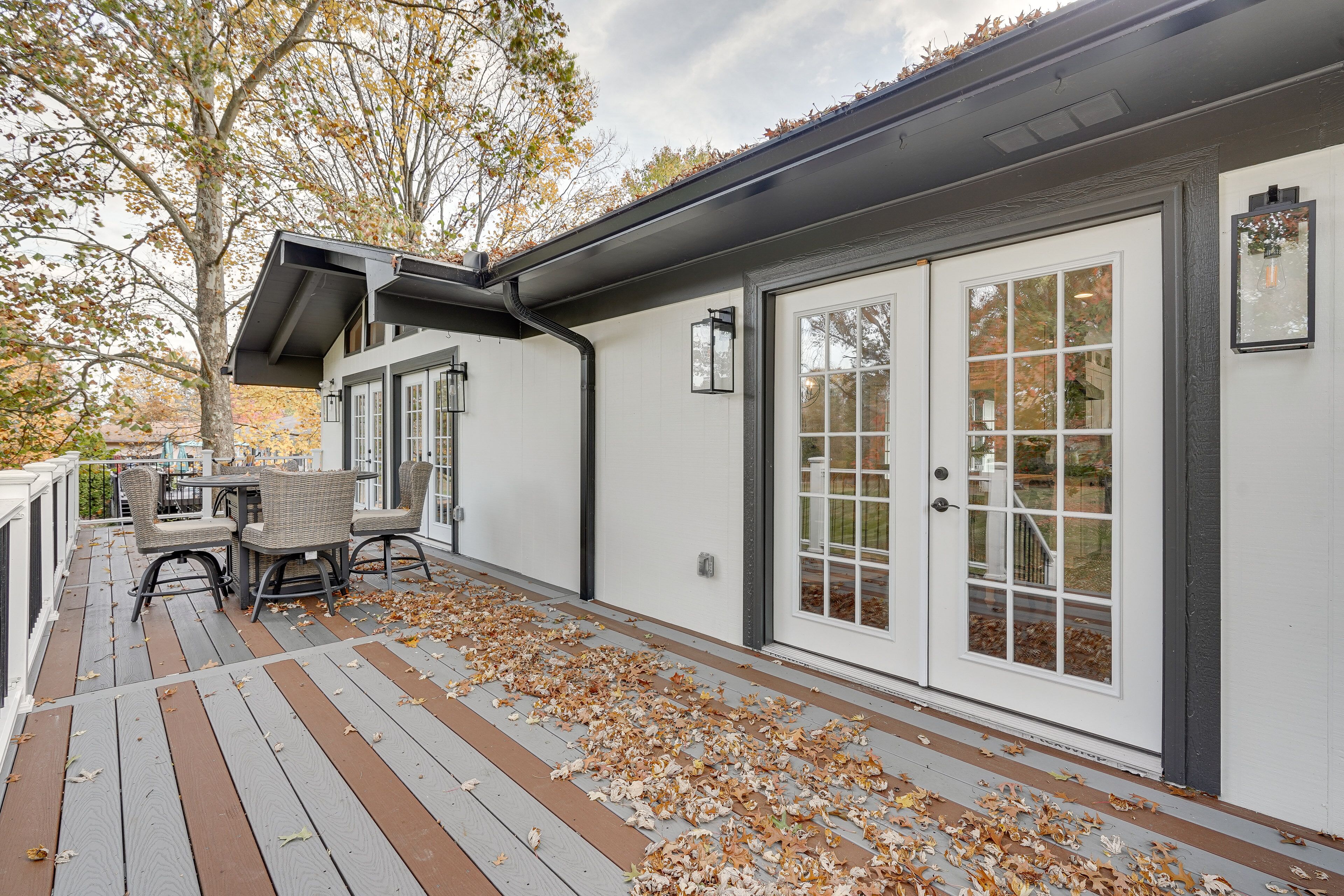 Une terrasse couverte avec un espace repas, une grande porte-fenêtre coulissante et un arbre aux feuilles d’automne.