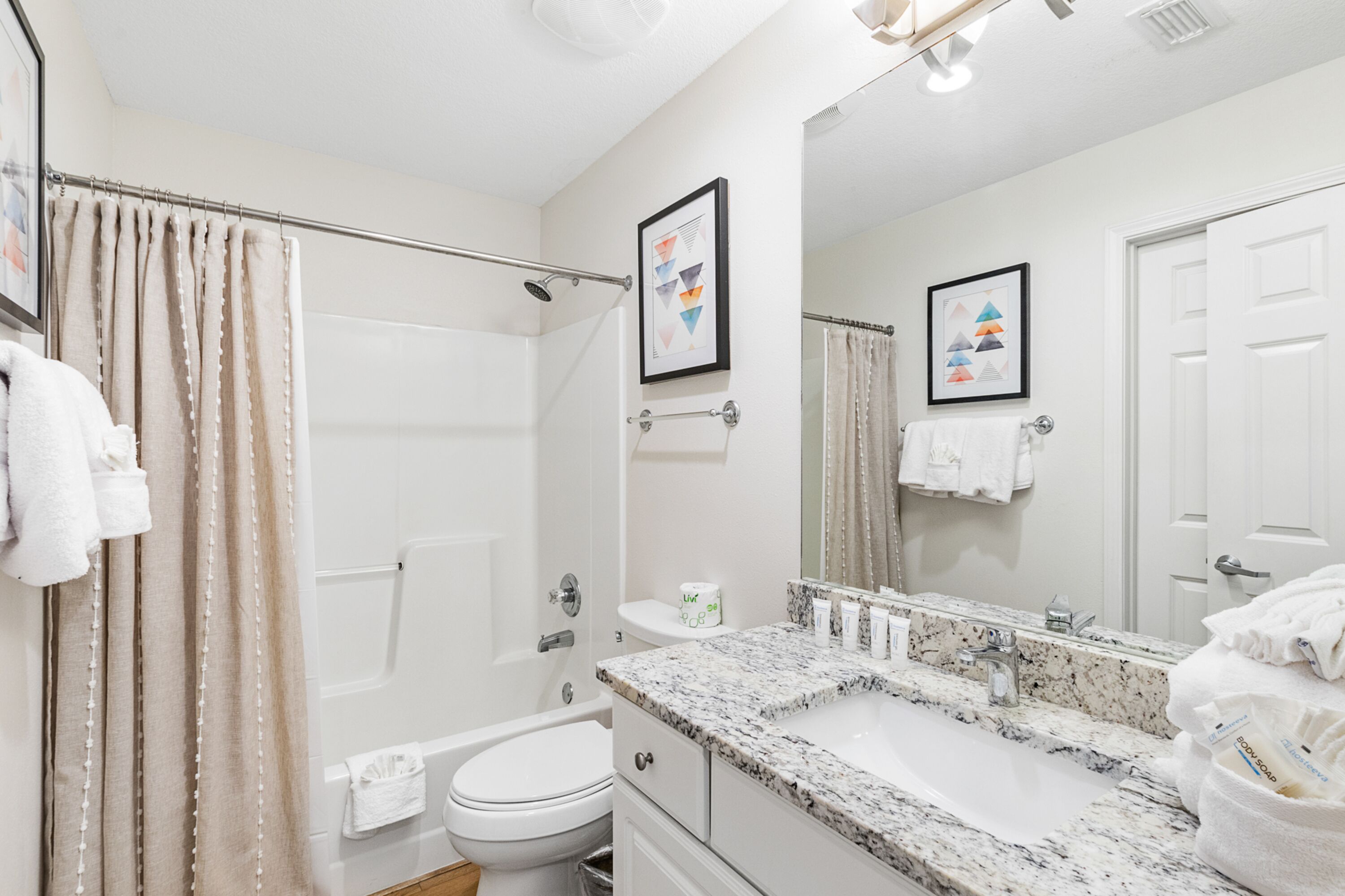 A bathroom with a shower, toilet, sink, and a large mirror.