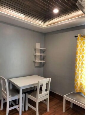 Ein Eckzimmer mit weißem Tisch und Stühlen, Holzboden und einer Decke mit Einbuchtungslampen.