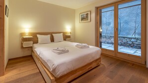 A bedroom with a wooden bed, white linens, two bedside lamps, a painting on the wall, and a view of a snowy outdoor area through large windows. - Montagnard 3 - Spa access (Haute-Nendaz)