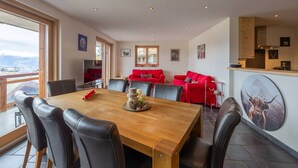 A dining area with a wooden table and leather chairs, a red sofa set, and a kitchen area with a stove and a large picture of a bull. - Montagnard 3 - Spa access (Haute-Nendaz)