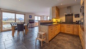 A modern kitchen with wooden cabinets, a dining area with a table and chairs, and large windows offering a mountain view. - Montagnard 3 - Spa access (Haute-Nendaz)