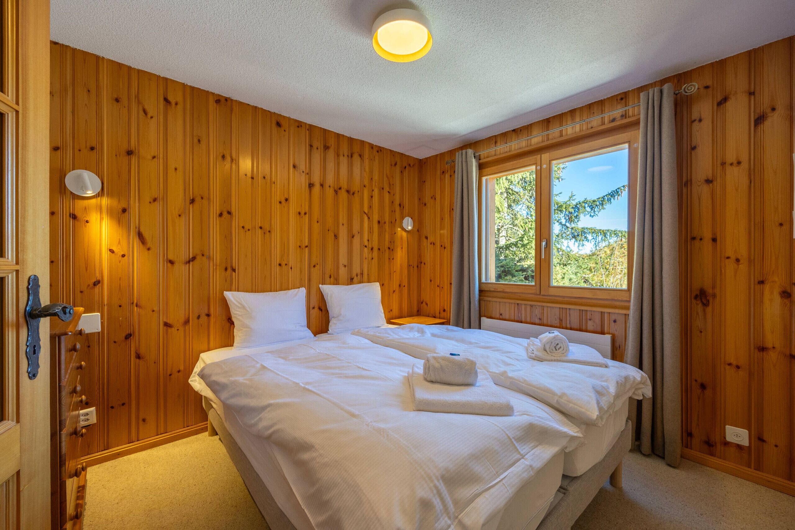A room with wooden walls, a large bed with white linens, a window with curtains, and a ceiling light.