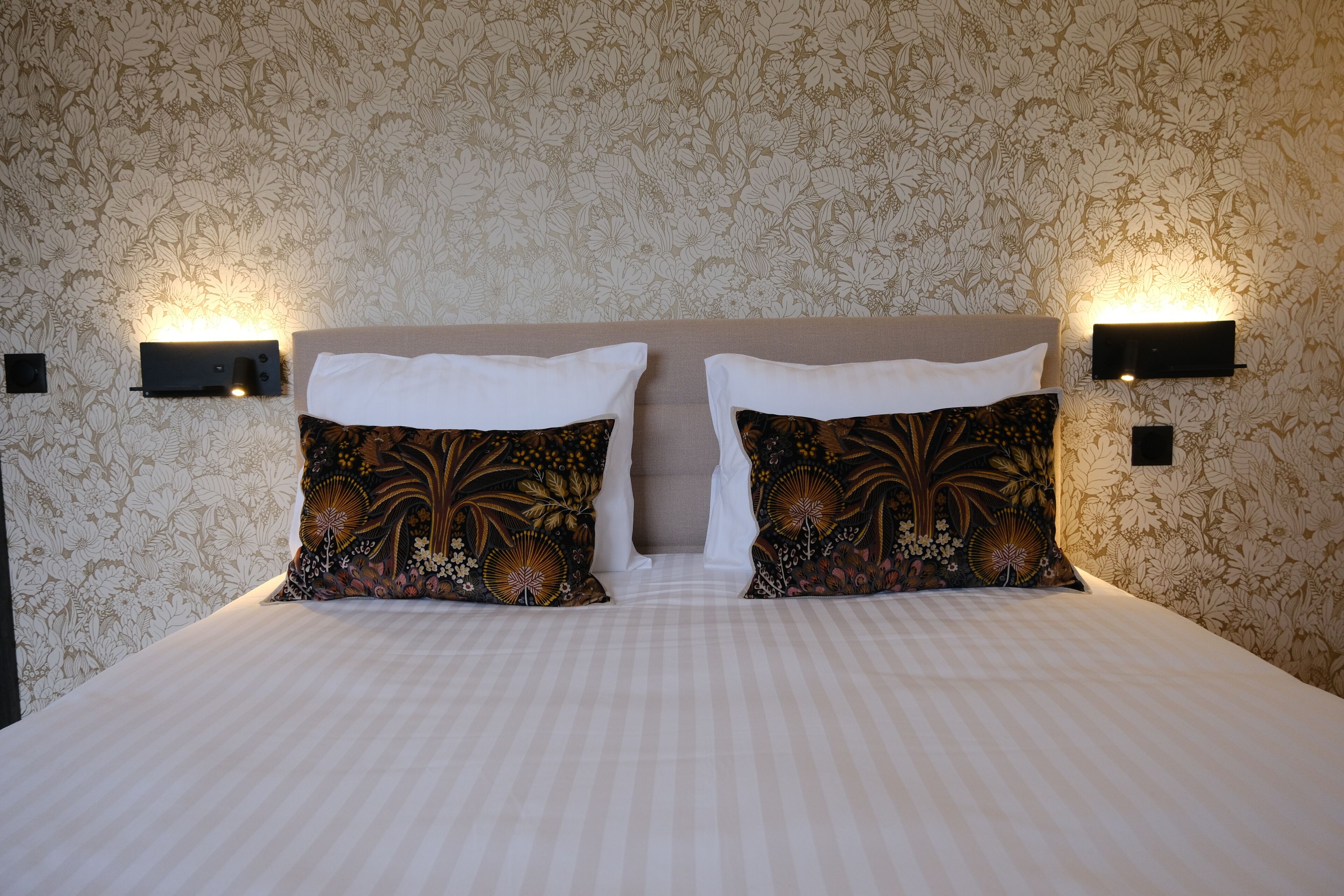 A hotel room with a large bed, two decorative pillows, and wall-mounted light fixtures.