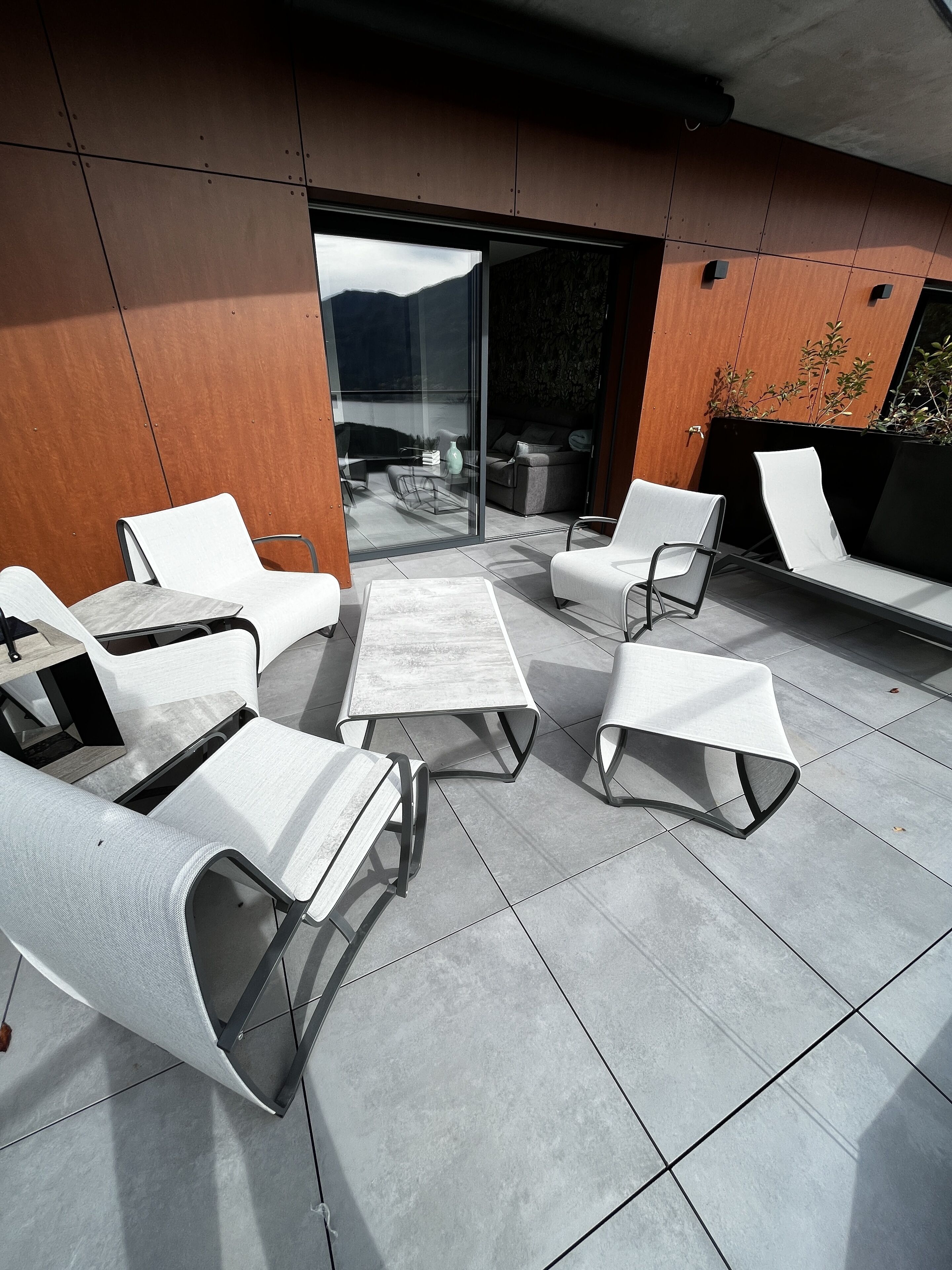 Un espace extérieur moderne avec des chaises blanches et une table, une porte vitrée donnant sur un balcon et un mur en bois.
