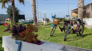 A garden area with a white bench, a bicycle, and a play structure in the background. - ★Case Playa ★ Parking Area (Balestrate)