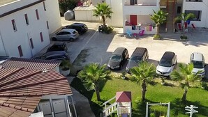 A residential area with multiple two-story buildings, a parking lot with several cars, and a small playground with a swing set. - ★Case Playa ★ Parking Area (Balestrate)