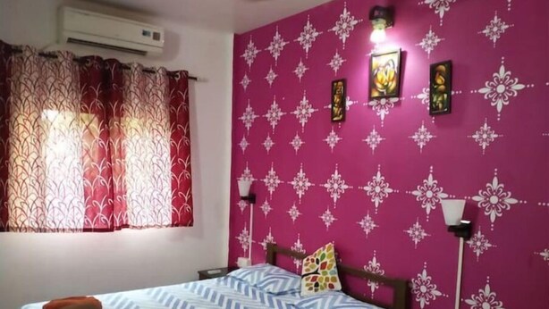 Ein Schlafzimmer mit Bett, Vorhängen, einer blumengemusterten Wand und einem Deckenventilator.