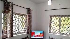 Ein Zimmer mit einer Couch, einem Fernseher und zwei Fenstern mit Metallgitter.