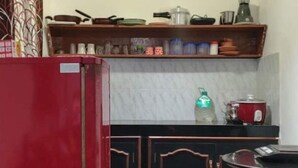 Eine Küche mit einem roten Kühlschrank, einer Arbeitsplatte mit verschiedenen Küchenutensilien und einem Regal darüber.