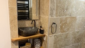 A bathroom with a stone sink, a mirror, a towel rack, and a shower area. - Gîte Dans les Cévennes (L'Estréchure)