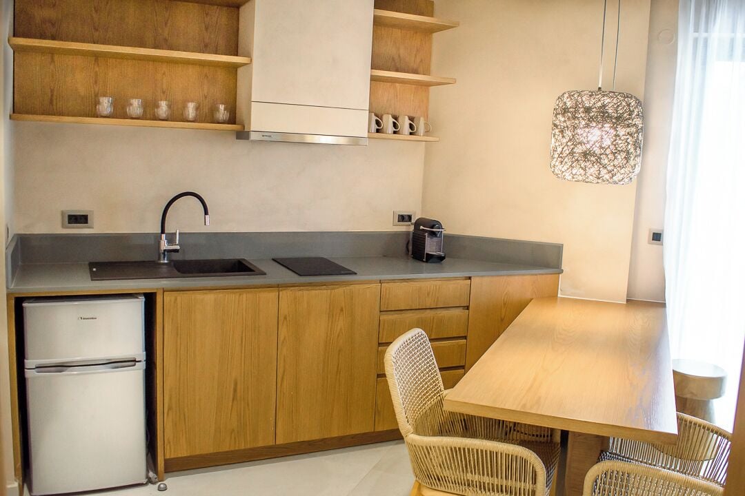 A compact kitchen with wooden cabinets, a built-in refrigerator, a sink, and a dining area with a table and wicker chairs.