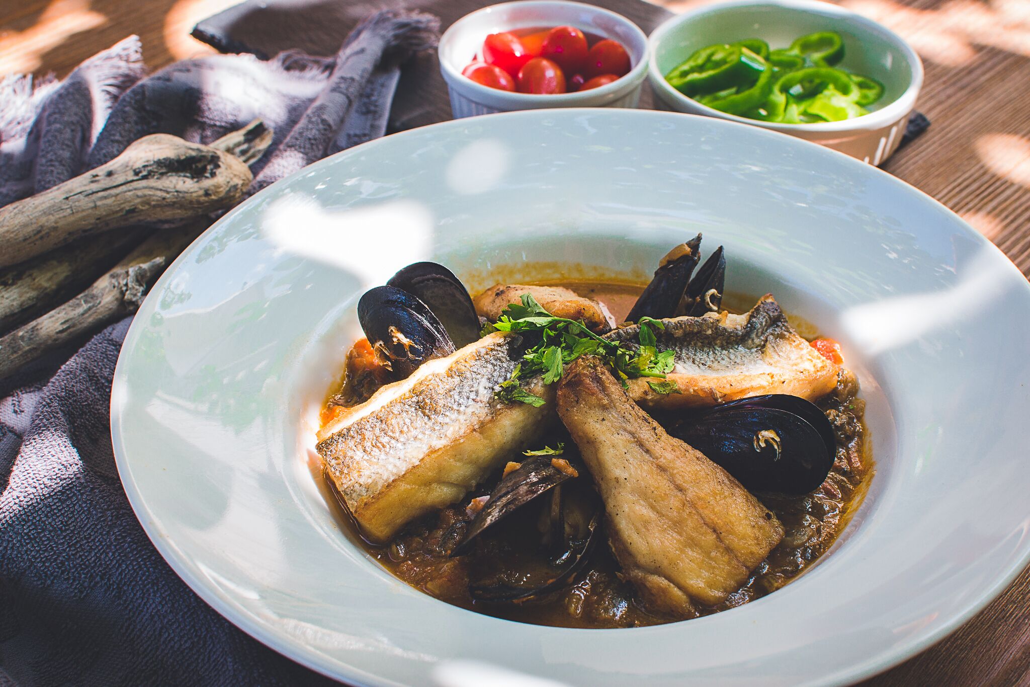 A seafood dish with mussels and fish, accompanied by a bowl of cherry tomatoes and green peppers.