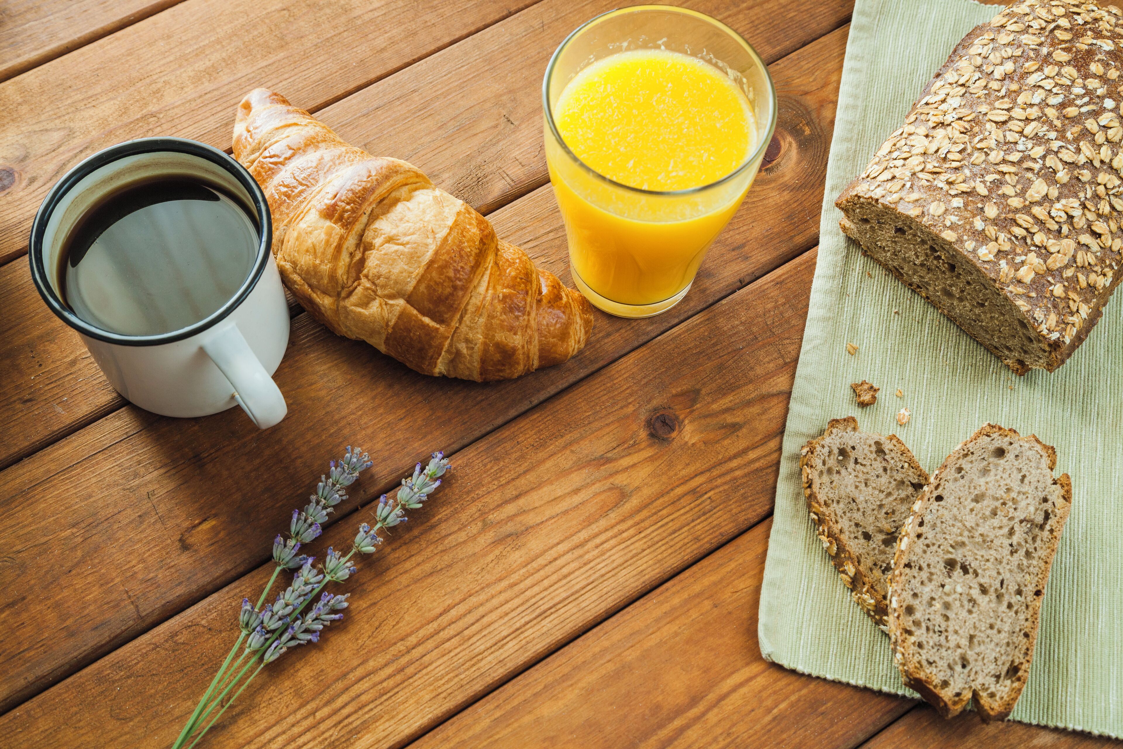 A wooden table with a croissant, a glass of orange juice, a mug of coffee, and slices of bread.