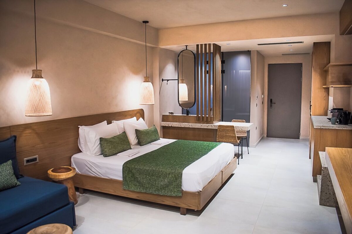 A modern hotel room with a wooden bed, a desk, and a bathroom visible through a glass door.