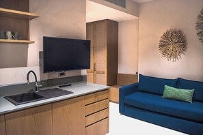 A modern kitchen with a built-in TV, wooden cabinets, and a blue sofa. - Panorama Hotel (Kissamos)