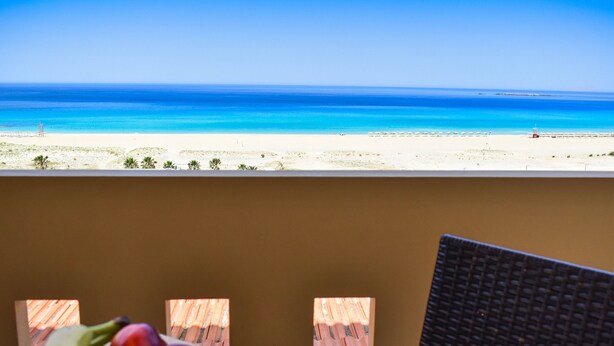 A balcony with a view of a beach and ocean. There is a table with fruits and a cup. - Panorama Hotel (Kissamos)