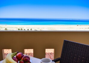 Un balcón con vistas a la playa y al océano. Hay una mesa con frutas y una taza.