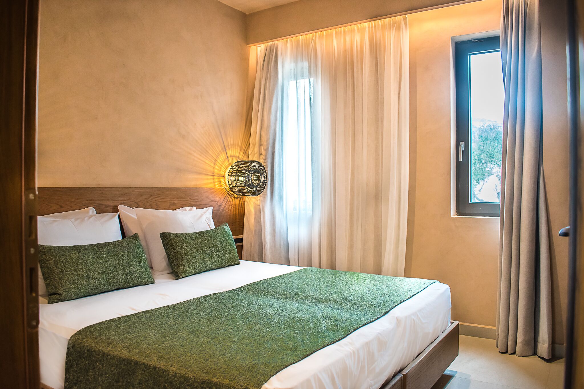 A neatly made bed with green bedding, a headboard, and a wall-mounted light fixture.