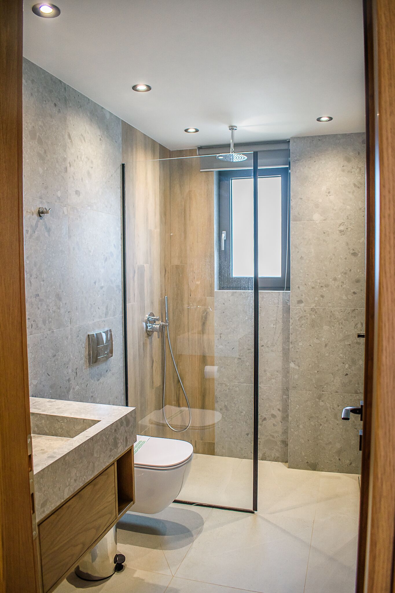 A modern bathroom with a glass-enclosed shower, a toilet, and a vanity with a marble countertop.