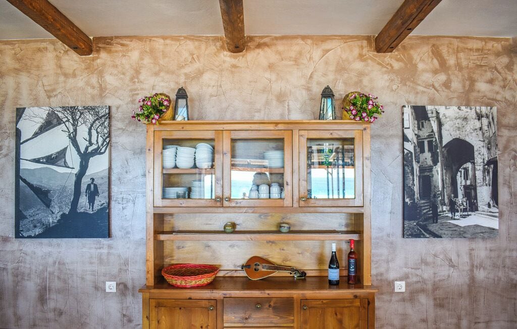 A rustic wooden cabinet with glass doors, a basket, a bottle, and two framed pictures on the wall.