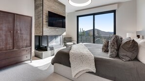 Een moderne slaapkamer met een groot bed, een open haard, een kledingkast en een balkon met uitzicht op de bergen.