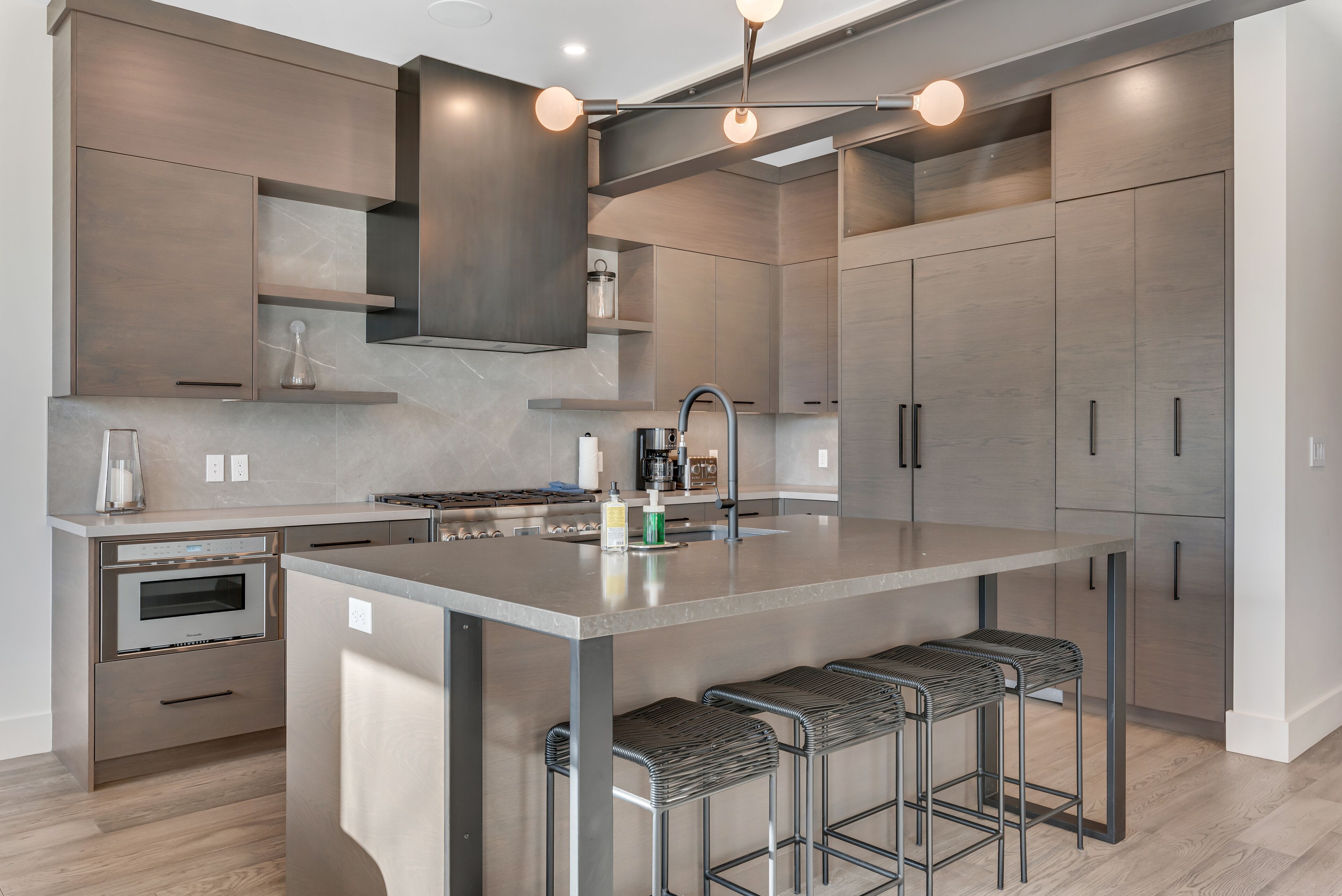 A modern kitchen with a central island, stainless steel appliances, and bar stools.