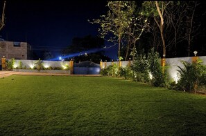 A well-lit outdoor area with a paved walkway, a gated entrance, and a grassy lawn. - Southern Universal Farm House (Vanur)