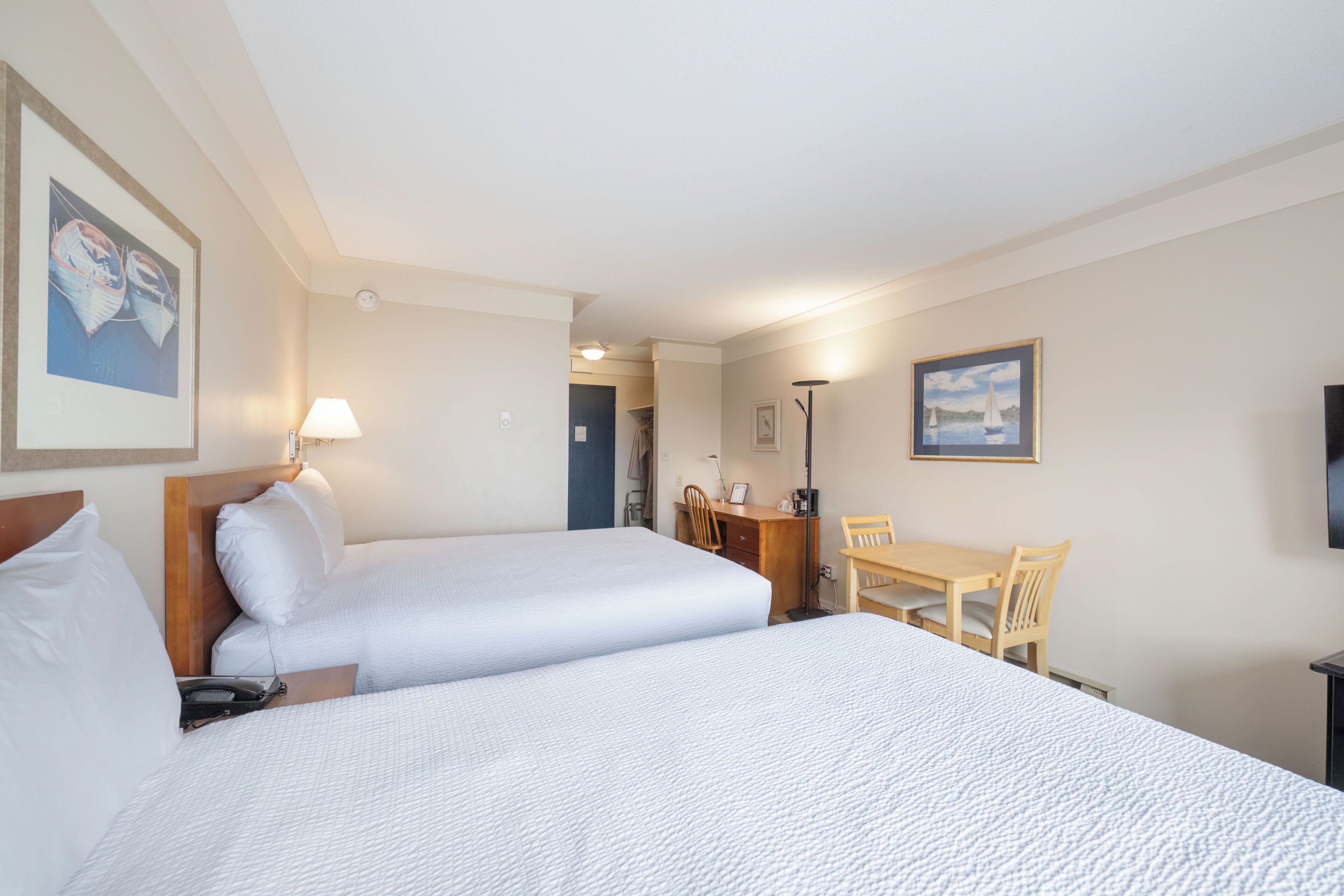 A hotel room with two beds, a desk, a chair, a lamp, and a TV.