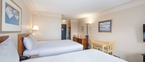 A hotel room with two beds, a desk, a chair, a lamp, and a TV.