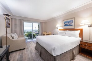 A hotel room with a large bed, a desk, a chair, a balcony with a view, and a painting on the wall. - Sidney Waterfront Inn & Suites (Sidney)