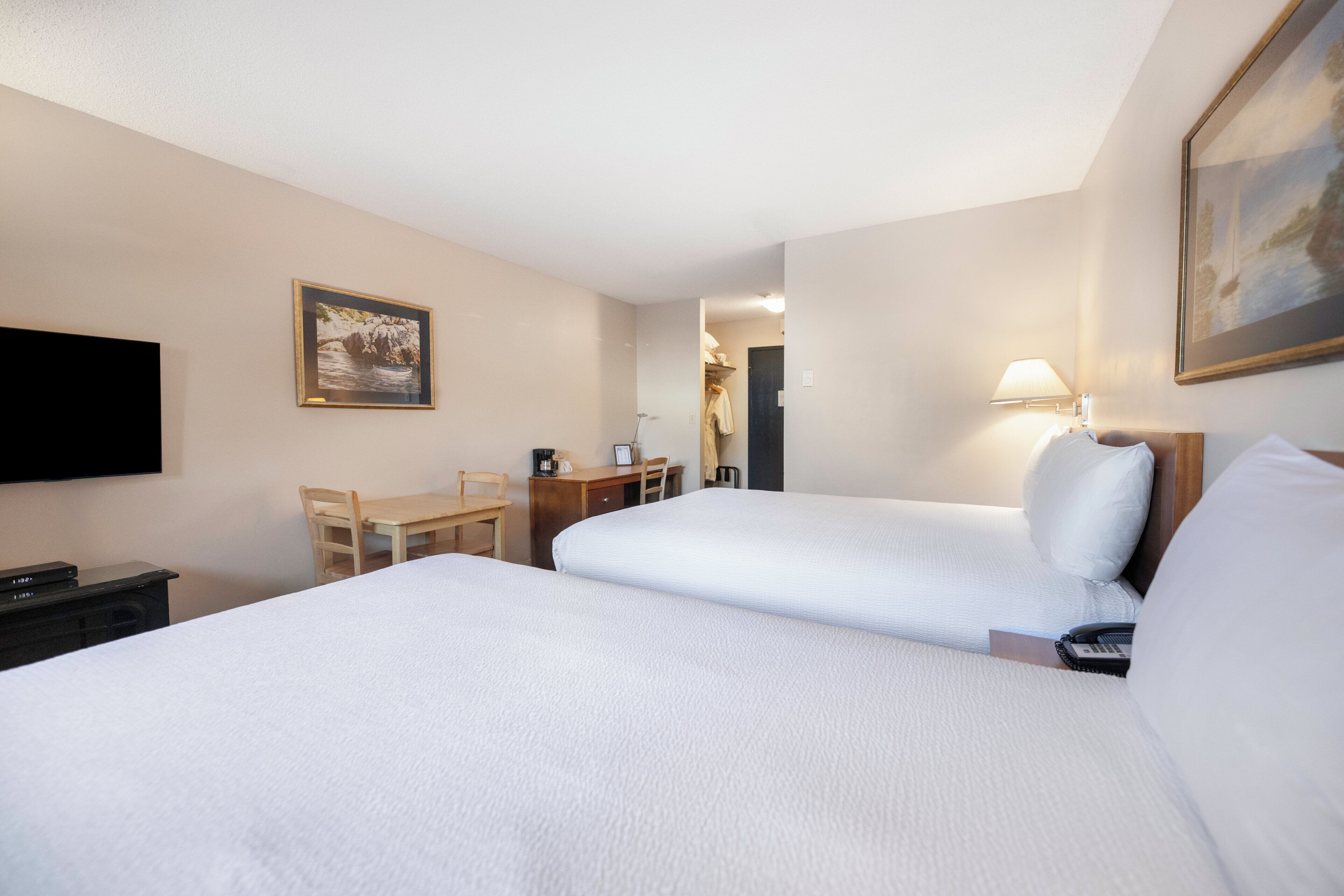 A hotel room with two beds, a desk, a chair, a TV, and a painting on the wall.