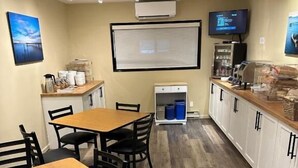 Kokoushuone, jossa on puinen pöytä ja tuolit, valkotaulu, ilmastointilaite, televisio ja pieni keittiöalue.