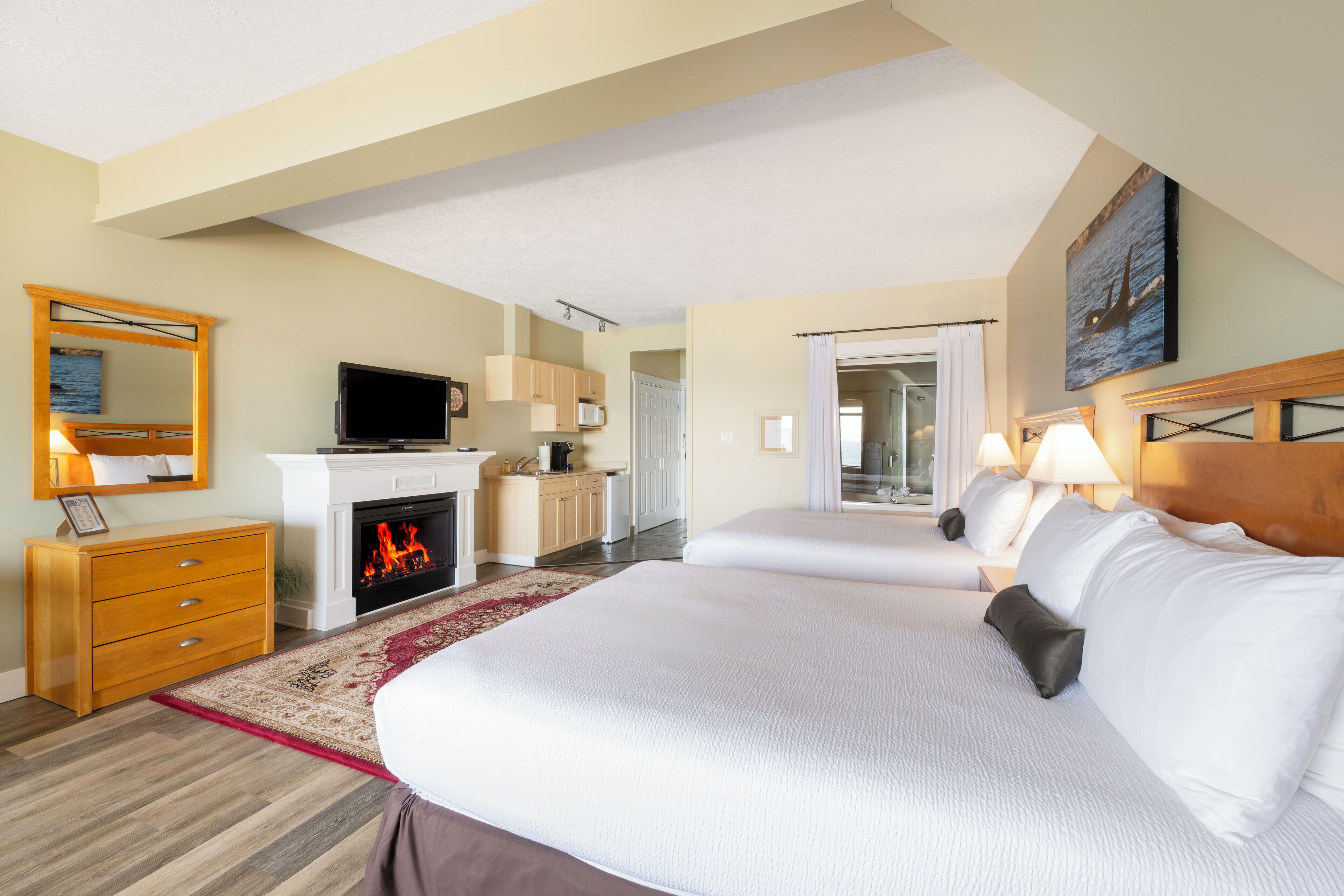 A hotel room with two beds, a fireplace, a television, and a view of the ocean through the window.