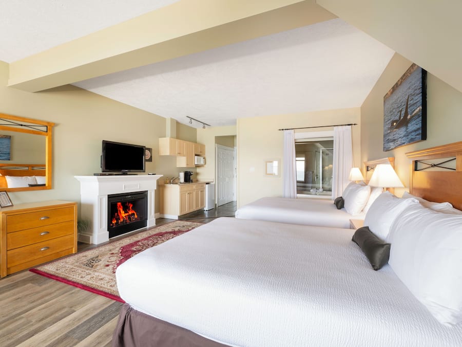 A hotel room with two beds, a fireplace, a television, and a view of the ocean through the window.