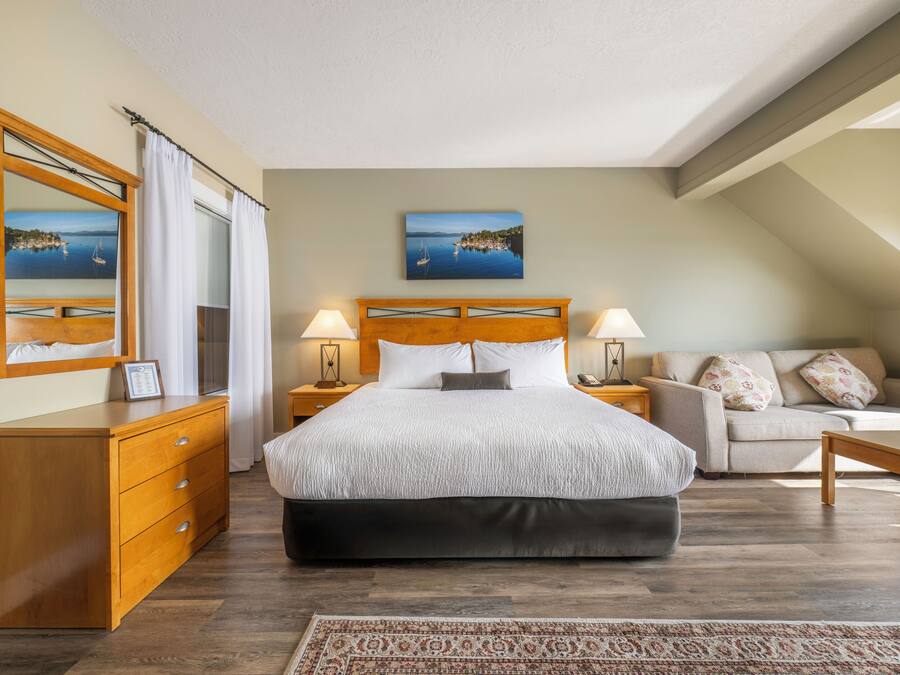 A bedroom with a large bed, a wooden dresser, a sofa, and a nightstand with lamps.