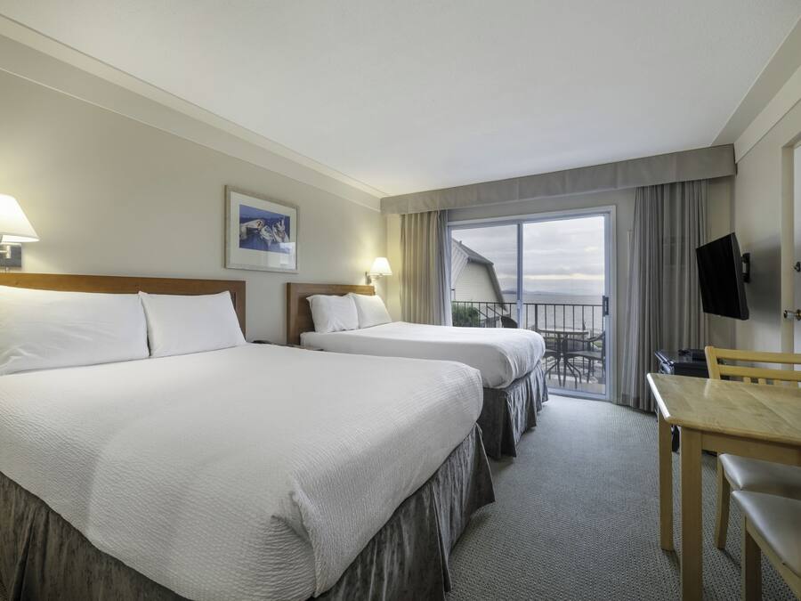 A hotel room with two beds, a desk, a TV, and a balcony with a view.